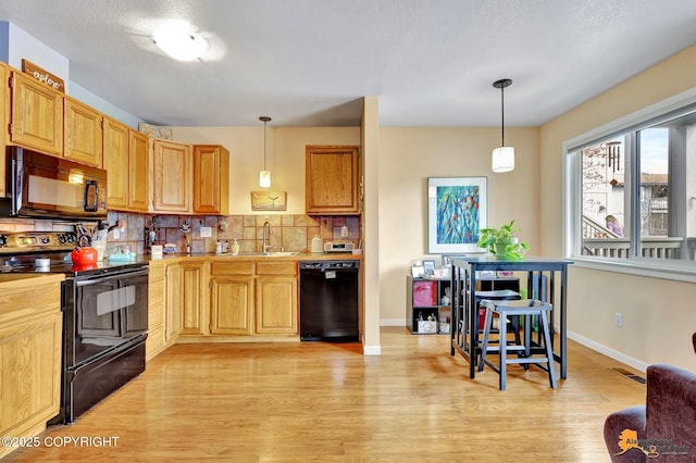 kitchen featuring decorative backsplash, a sink, light countertops, black appliances, and light wood-style flooring