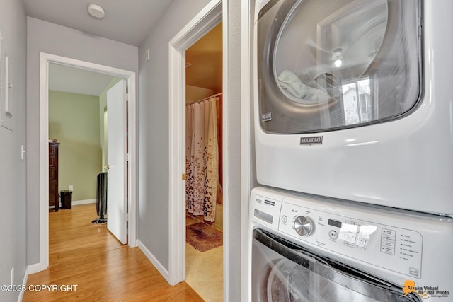 laundry area featuring baseboards, stacked washer / drying machine, light wood-type flooring, and laundry area