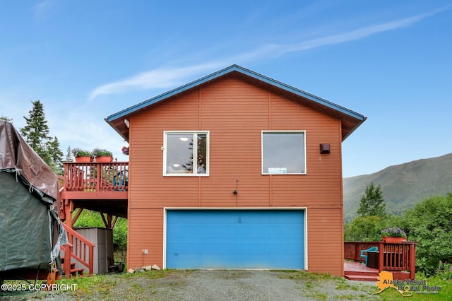 back of property featuring an attached garage, a deck with mountain view, and gravel driveway