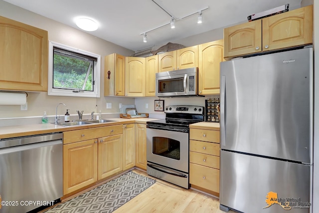 kitchen featuring light brown cabinets, light wood-type flooring, light countertops, a sink, and appliances with stainless steel finishes