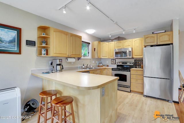 kitchen featuring track lighting, light brown cabinets, stainless steel appliances, and a peninsula
