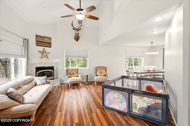 living room featuring wood finished floors, ceiling fan, high vaulted ceiling, a glass covered fireplace, and baseboards