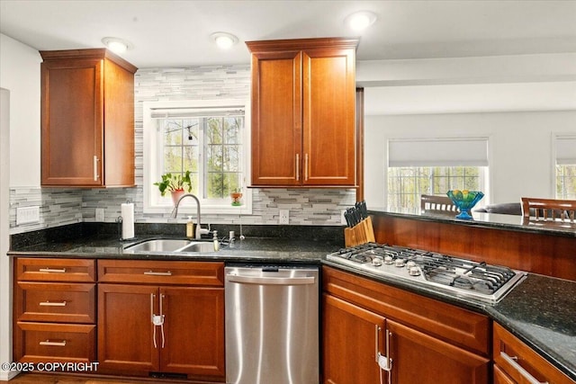kitchen with stainless steel appliances, a sink, backsplash, and dark stone counters