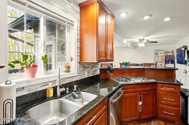 kitchen featuring a sink, stainless steel appliances, a peninsula, a ceiling fan, and decorative backsplash