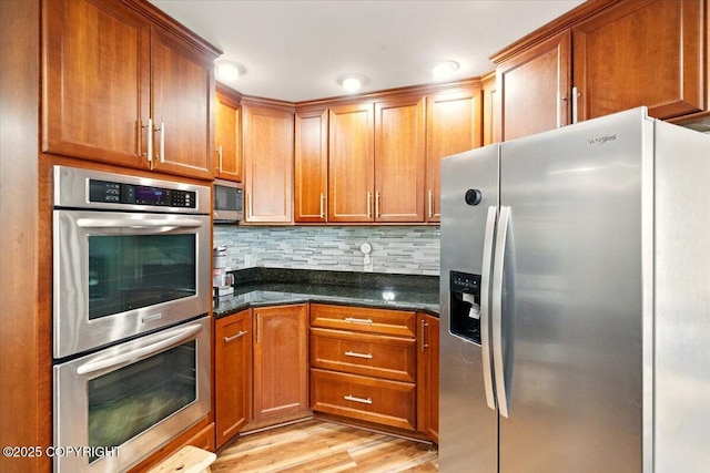 kitchen with appliances with stainless steel finishes, decorative backsplash, light wood-type flooring, and brown cabinets