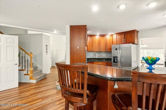 kitchen with stainless steel refrigerator with ice dispenser, a breakfast bar area, backsplash, light wood-type flooring, and brown cabinetry