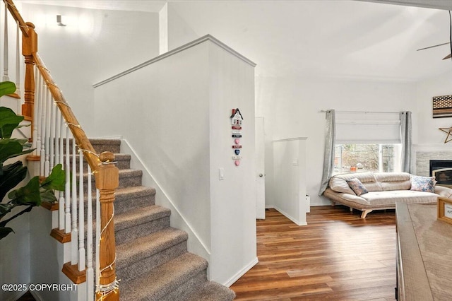stairs featuring wood finished floors, a glass covered fireplace, baseboards, and ceiling fan
