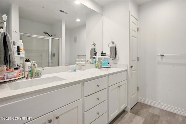 bathroom featuring wood finished floors, a shower stall, double vanity, recessed lighting, and baseboards