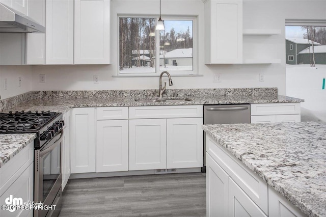 kitchen featuring under cabinet range hood, a sink, stainless steel range with gas cooktop, white cabinets, and open shelves