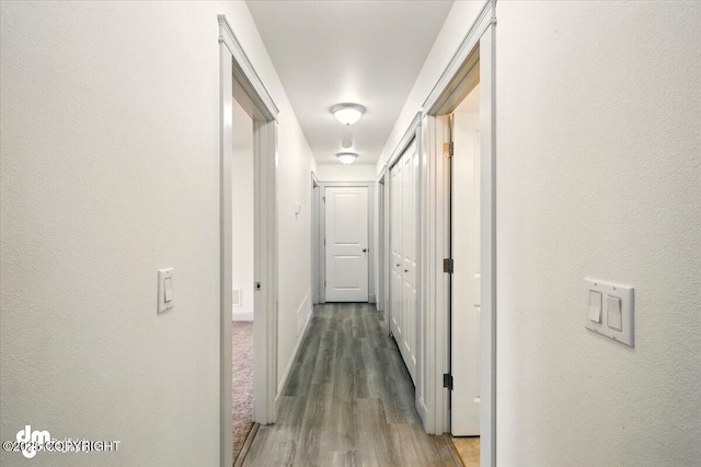 corridor featuring wood finished floors, baseboards, and a textured wall