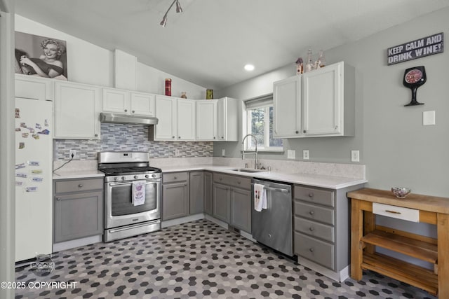 kitchen featuring appliances with stainless steel finishes, a sink, gray cabinetry, vaulted ceiling, and light countertops