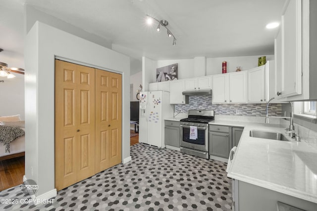 kitchen featuring stainless steel range with gas stovetop, a sink, under cabinet range hood, white refrigerator with ice dispenser, and decorative backsplash