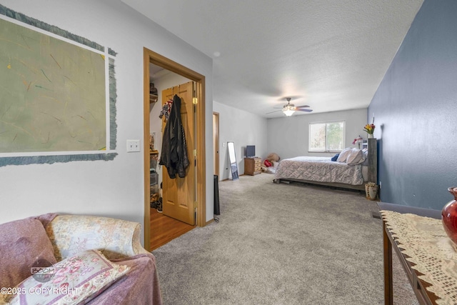 carpeted bedroom with a walk in closet, ceiling fan, baseboards, and a textured ceiling