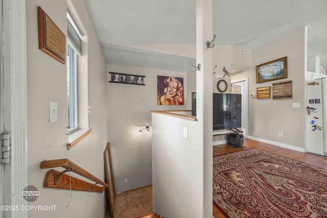 hall with wood finished floors, healthy amount of natural light, baseboards, and vaulted ceiling