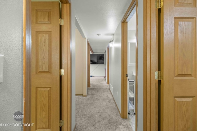 hallway featuring light colored carpet and baseboards