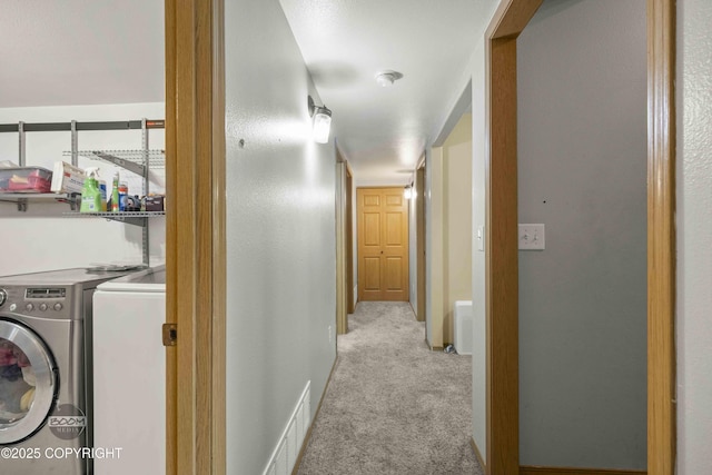 hallway with washing machine and clothes dryer, light carpet, and baseboards