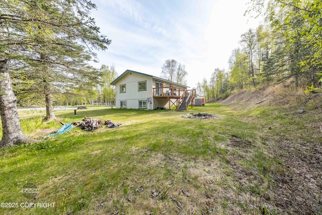 view of grassy yard featuring stairs, a wooden deck, and an outdoor fire pit