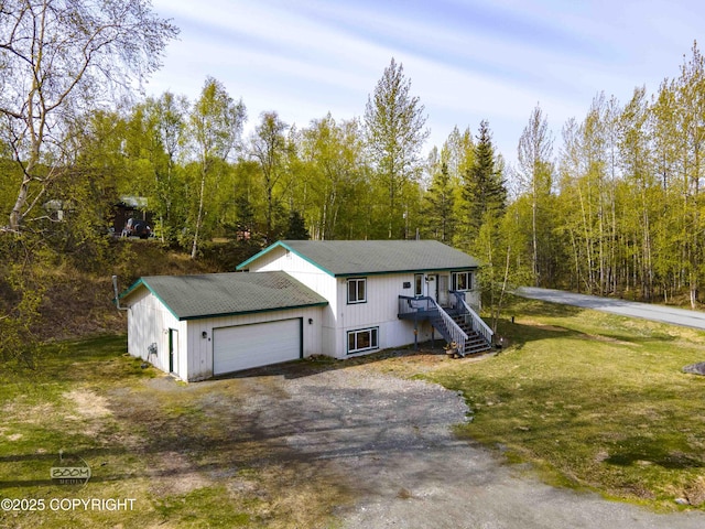 view of front of house featuring stairway, a front yard, dirt driveway, a garage, and a forest view