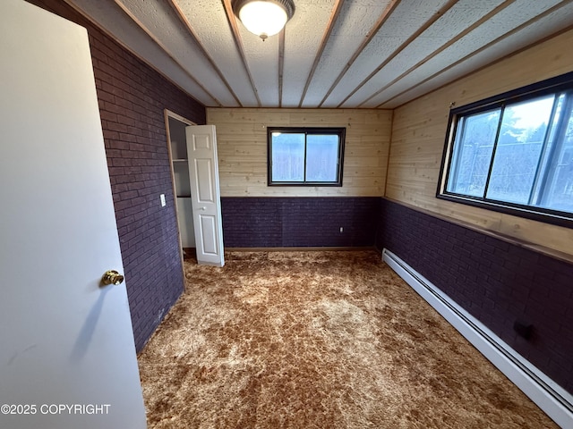 carpeted empty room featuring plenty of natural light, a baseboard heating unit, and brick wall