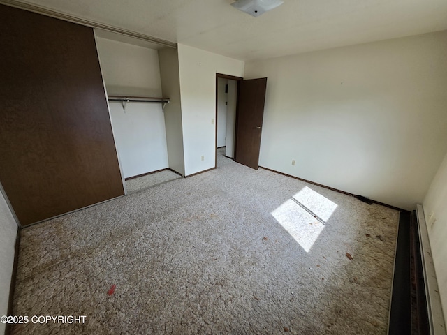 unfurnished bedroom featuring a closet, baseboards, carpet flooring, and a baseboard heating unit