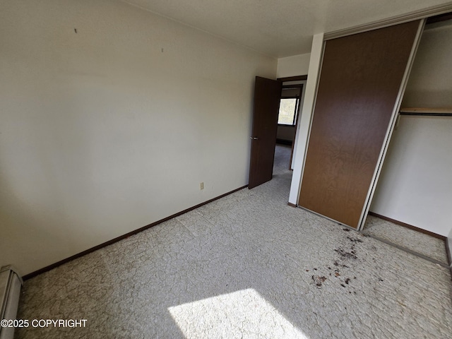 unfurnished bedroom featuring carpet floors, baseboards, baseboard heating, and a closet