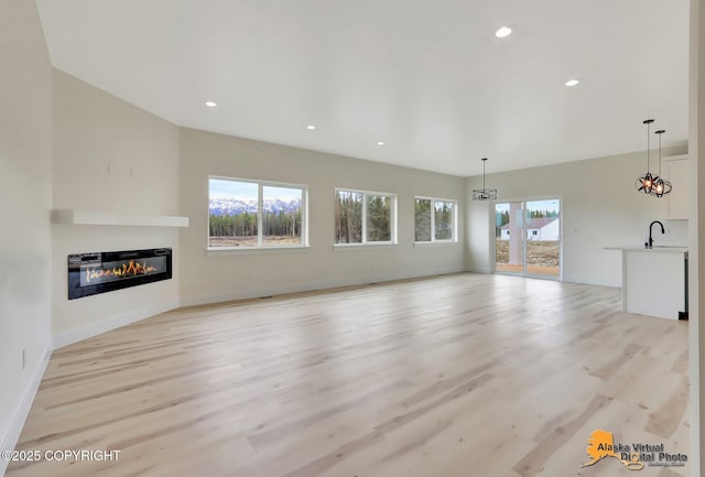 unfurnished living room with a sink, a glass covered fireplace, light wood-style flooring, recessed lighting, and baseboards