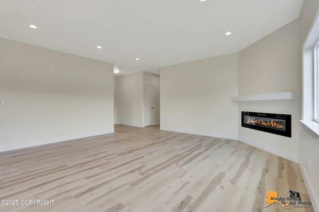 unfurnished living room featuring recessed lighting, a glass covered fireplace, and light wood finished floors