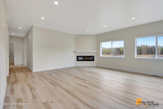 unfurnished living room with light wood-style floors, a glass covered fireplace, recessed lighting, baseboards, and visible vents