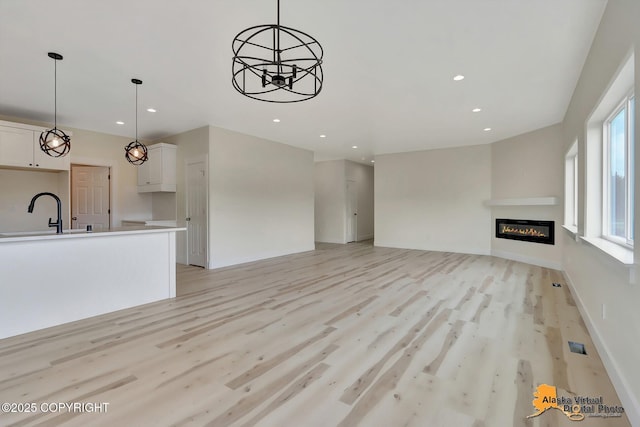 unfurnished living room with light wood-type flooring, a sink, a glass covered fireplace, and recessed lighting