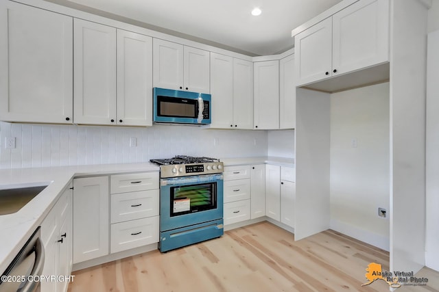 kitchen with white cabinets, light stone countertops, appliances with stainless steel finishes, light wood finished floors, and decorative backsplash