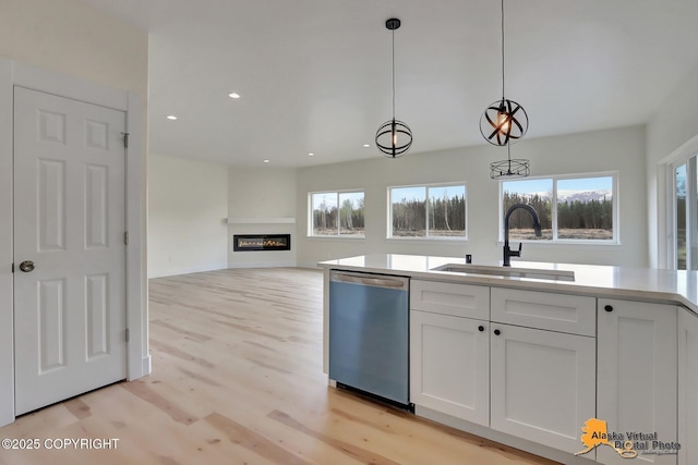 kitchen featuring decorative light fixtures, light wood-type flooring, dishwasher, a sink, and white cabinets
