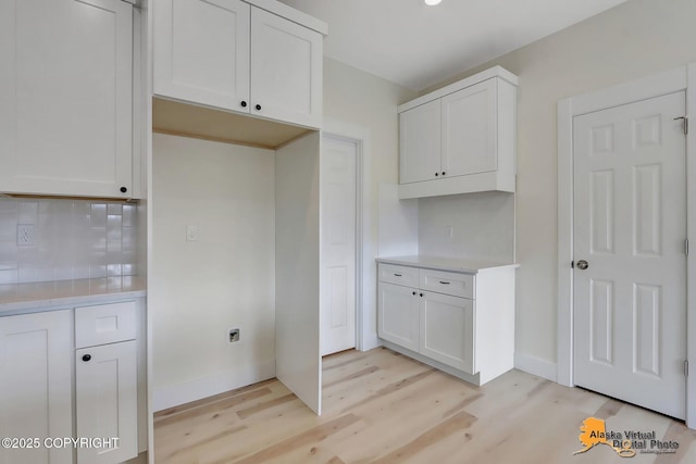 kitchen with white cabinets, decorative backsplash, and light wood finished floors