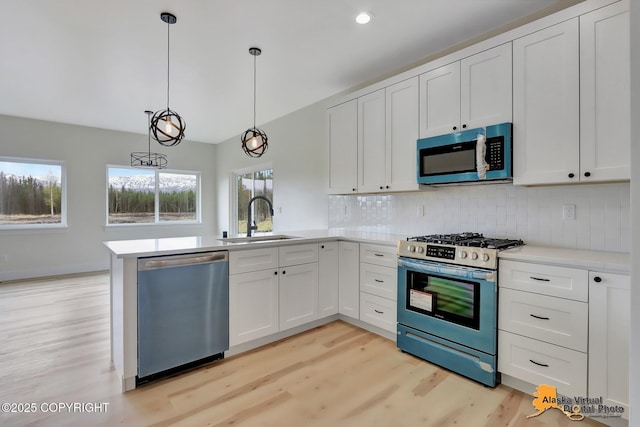 kitchen featuring a sink, light wood finished floors, stainless steel appliances, a peninsula, and decorative backsplash