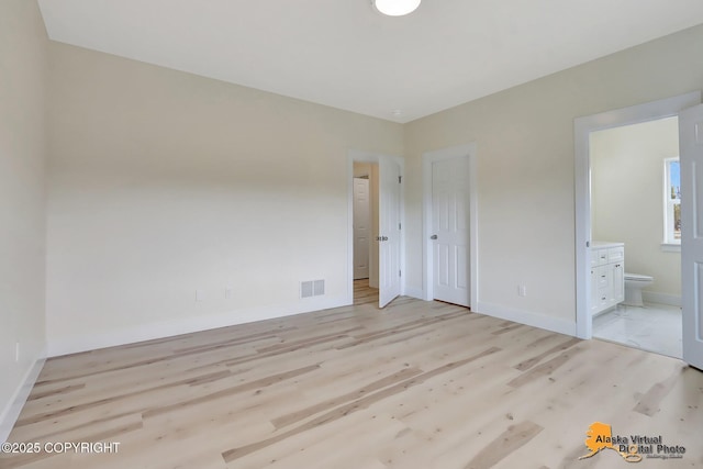 unfurnished bedroom with baseboards, ensuite bathroom, light wood finished floors, and visible vents