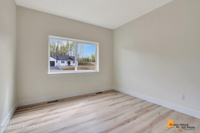 empty room with baseboards, visible vents, and wood finished floors