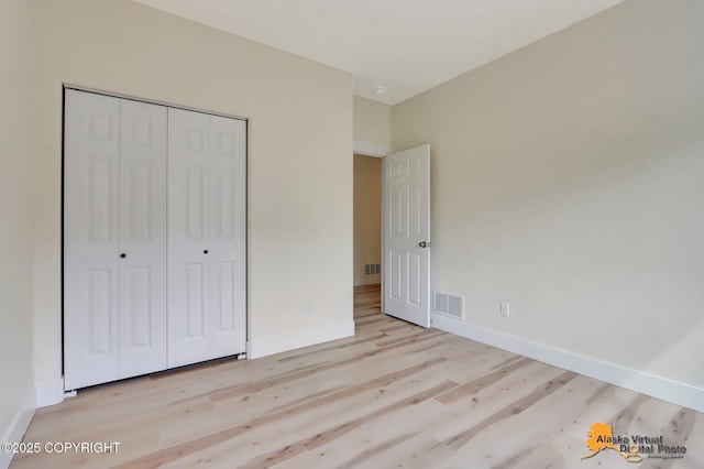 unfurnished bedroom featuring baseboards, a closet, wood finished floors, and visible vents