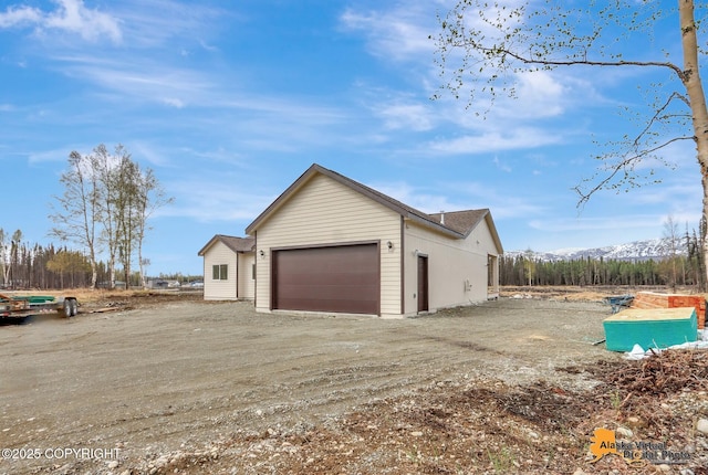 view of property exterior featuring dirt driveway, a mountain view, and a garage
