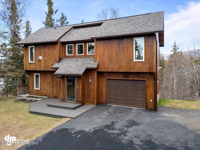 chalet / cabin with a shingled roof, an attached garage, a front lawn, and aphalt driveway