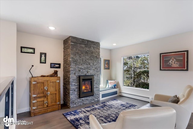 living area with a baseboard heating unit, baseboards, a fireplace, and wood finished floors