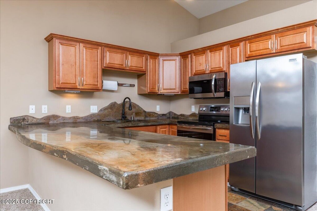 kitchen with brown cabinetry, a sink, a peninsula, dark stone counters, and stainless steel appliances