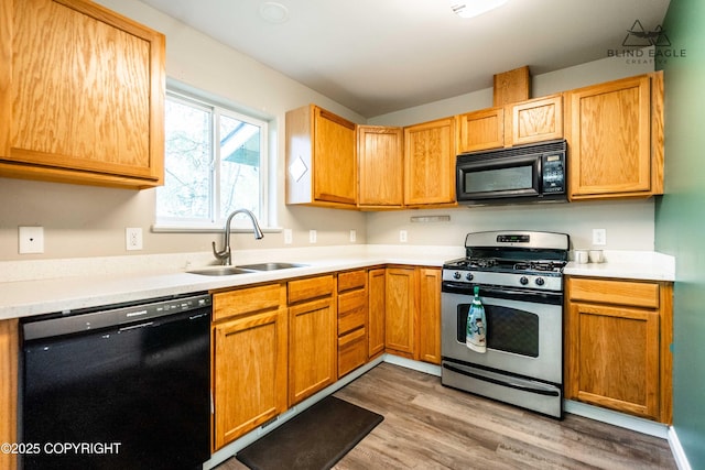 kitchen with black appliances, a sink, light wood finished floors, and light countertops