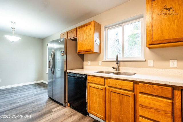 kitchen with black dishwasher, a sink, light countertops, light wood-style floors, and brown cabinets
