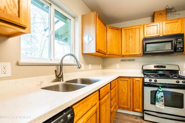 kitchen featuring black appliances, a sink, light countertops, and wood finished floors