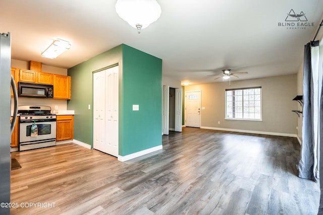 kitchen with stainless steel gas range, black microwave, light wood finished floors, and ceiling fan