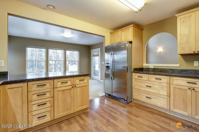 kitchen with light wood finished floors, light brown cabinets, dark stone counters, a peninsula, and stainless steel refrigerator with ice dispenser