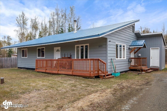 view of front of property with a deck, fence, metal roof, and a front yard