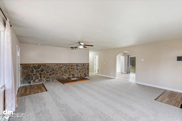 unfurnished living room with carpet floors, arched walkways, and ceiling fan