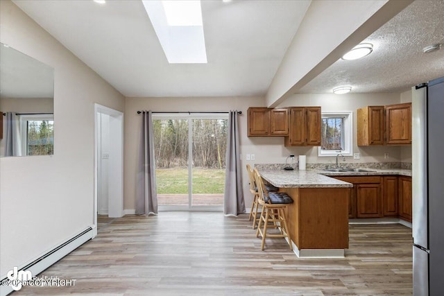 kitchen with brown cabinetry, a baseboard radiator, a peninsula, and a breakfast bar