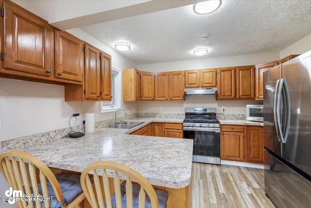 kitchen with a sink, light countertops, stainless steel appliances, a peninsula, and under cabinet range hood