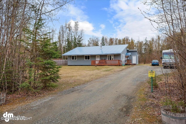 ranch-style house with fence, a deck, a front yard, driveway, and metal roof